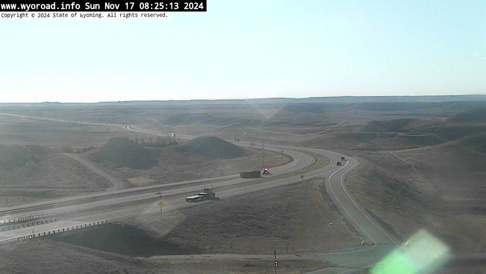 Picture of a highway in Wyoming with a truck tipped on its side from the wind. It is blocking a lane of traffic. 