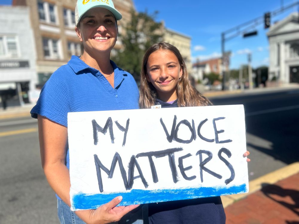Smiling mom & daughter hold “My Voice Matters” sign. 