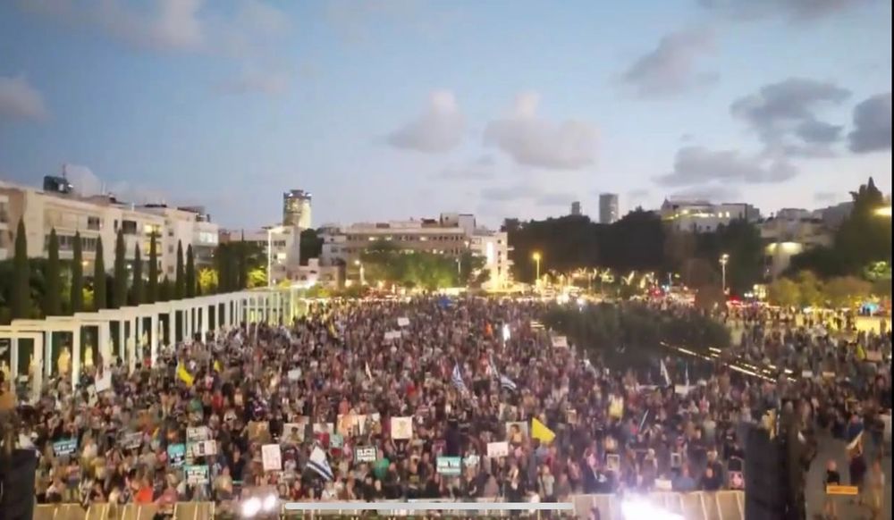 photo of thousands of protesters at dusk holding posters with clouds overhead.