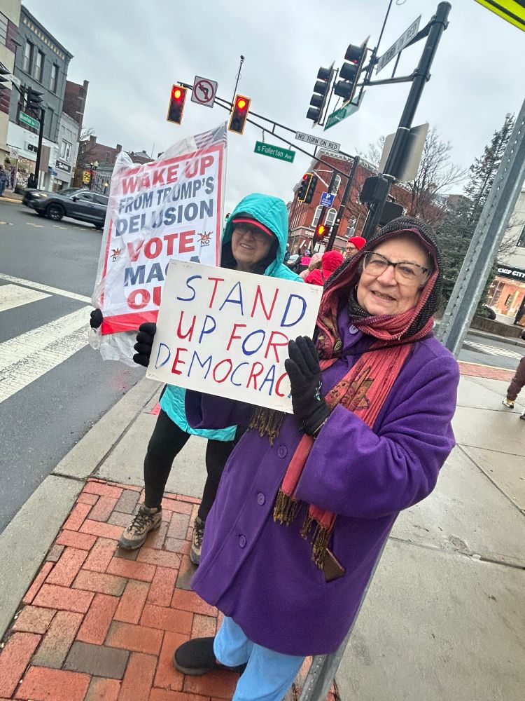 Two women in raincoats with Stand Up for Democracy sign 