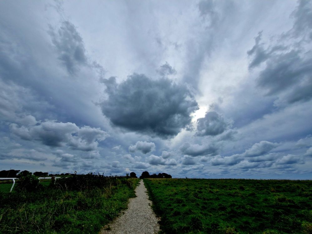 A dark grey cloud with light sun rays behind. Grassy land with a foot path in middle.