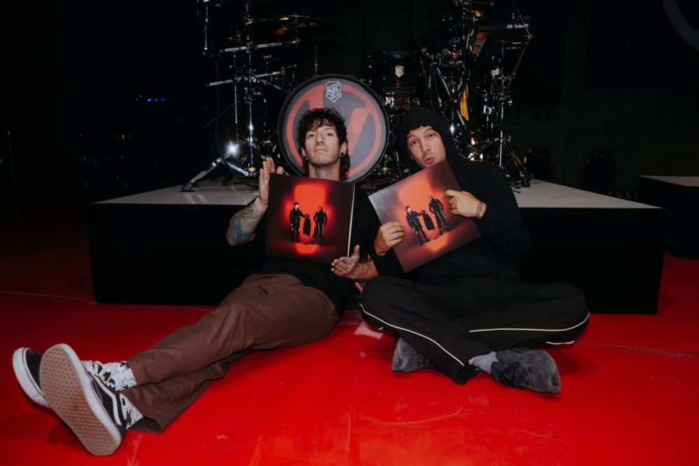 Tyler Joseph and Josh dun sitting in front of a drum set holding their new album "breach" 
