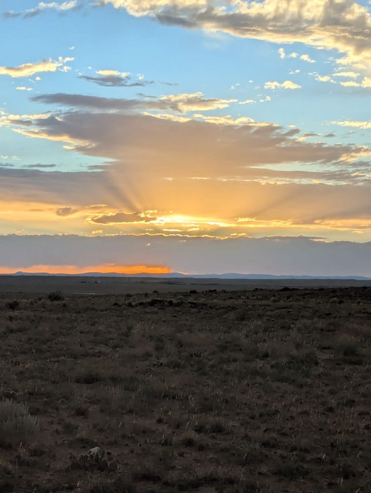Sunset view over desert scrub. Sunbeams shine through the clouds with blue sky above.  