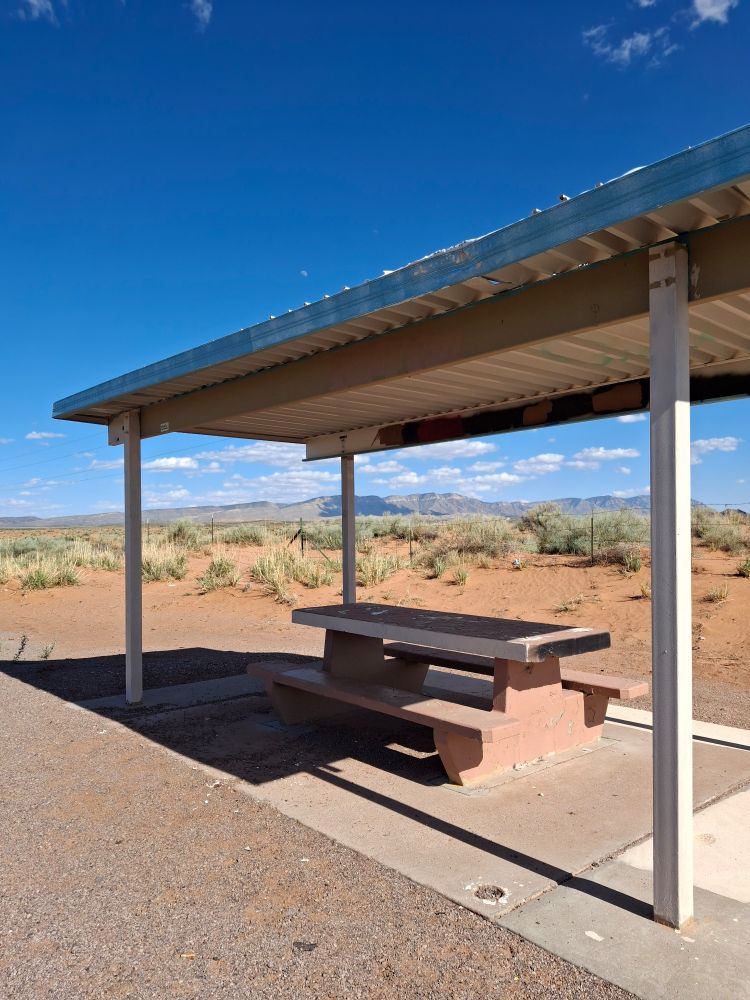 A picnic table under a shade structure with  New Mexico mountains in the background. 