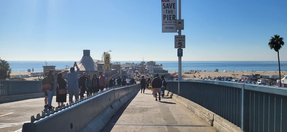 A view of the pier in Santa Monica, a massive crowd of people, very lively and sunny
