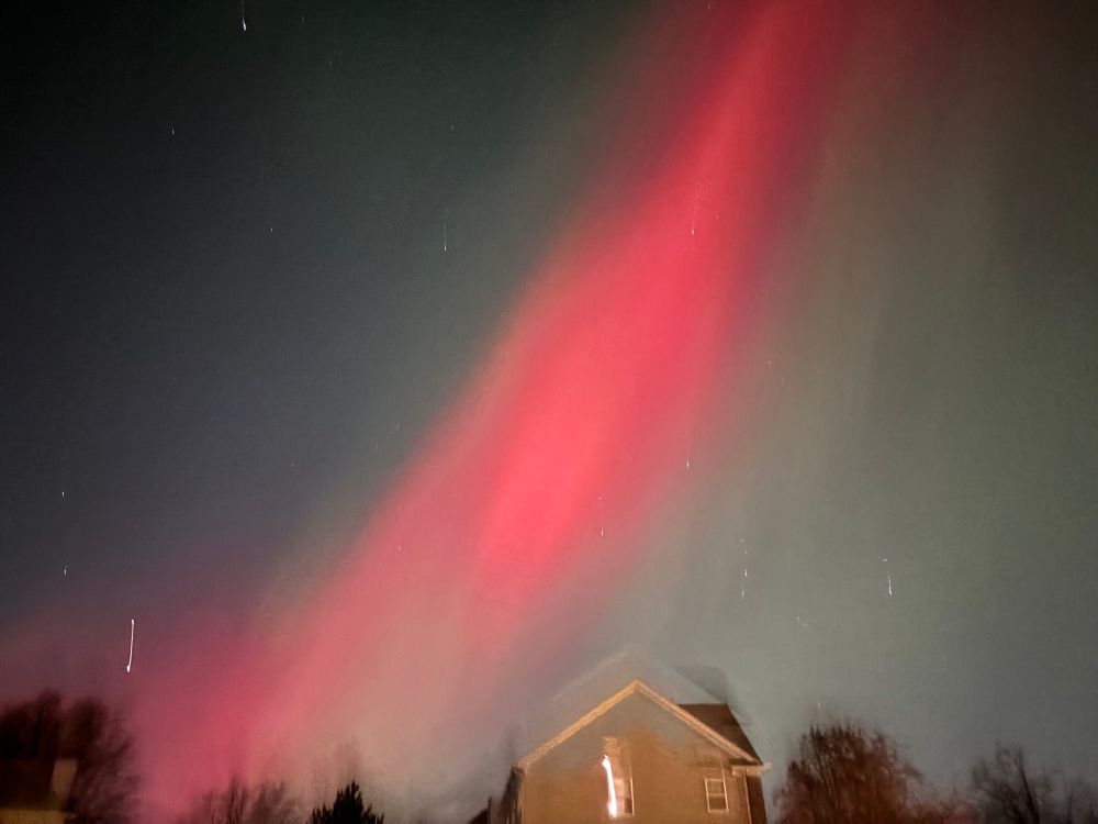 Night sky, slightly blurry. A bright red streak of Aurora Borealis cuts across the sky from upper right to lower left.