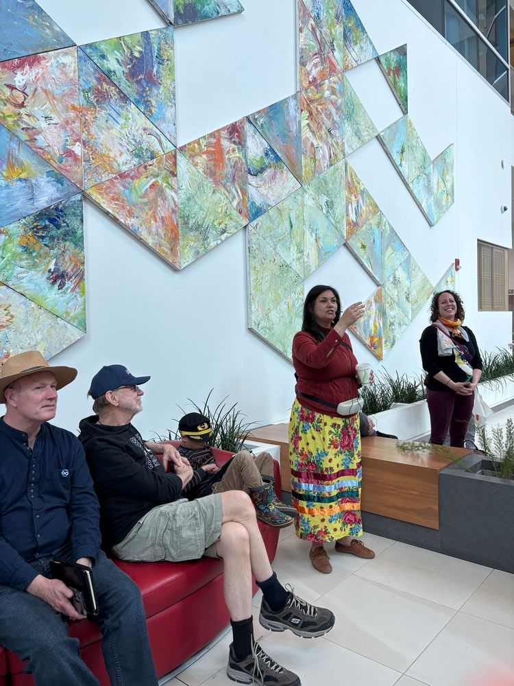 Tour guide in ribbon skirt talking in front of artwork.