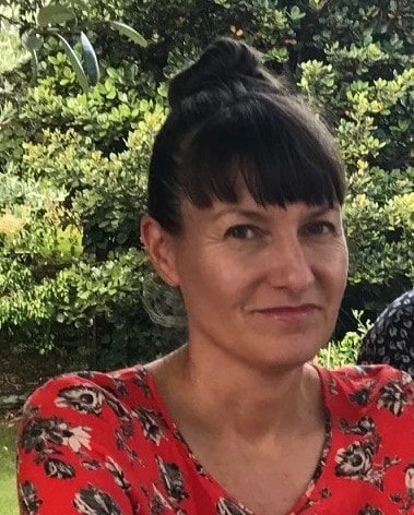 Photo of author Katie Furze in a red flowered top with green bushes and trees behind her.