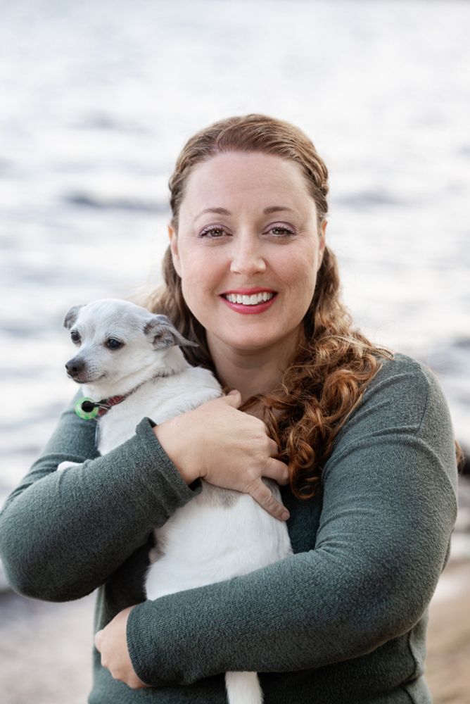 Photo of author Stephanie Gibeault smiling and holding a dog on a beach with gray waves in the background.