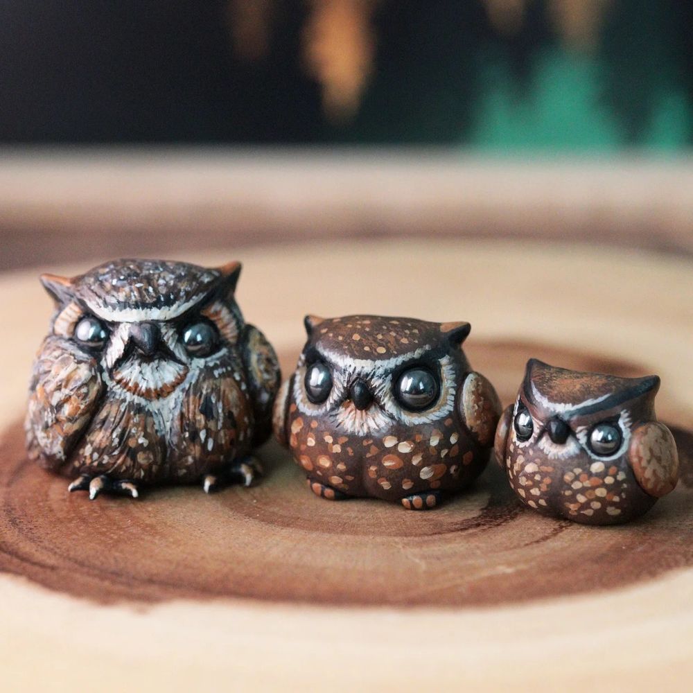 3 small owl figurines lined up on a wood round 