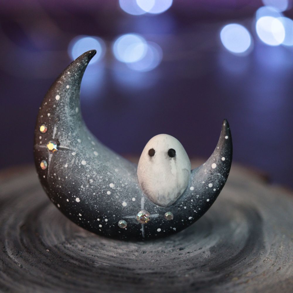 A sparkly black crescent moon figurine with a tiny ghost sat upon it
