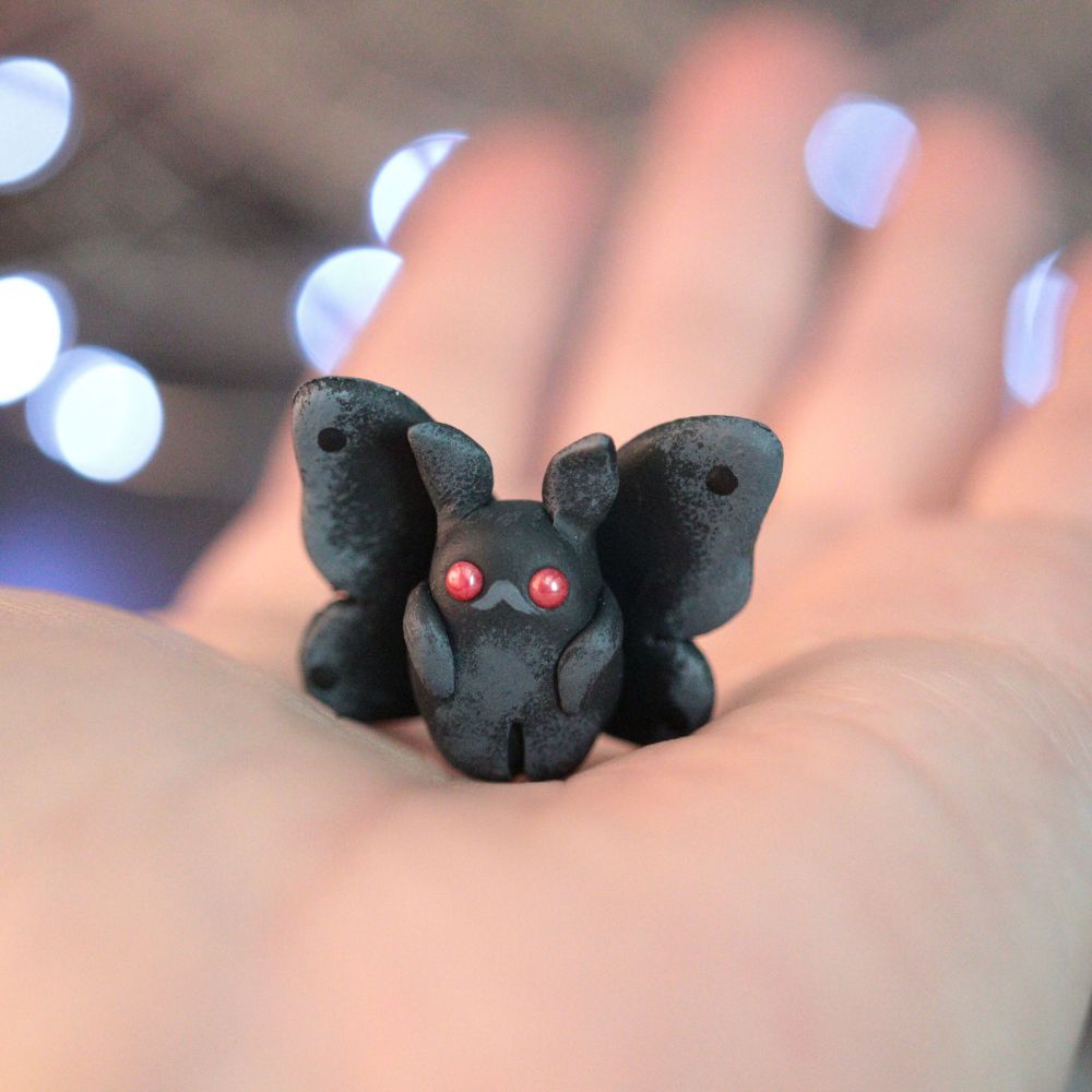 A hand holding a tiny mothman figurine 