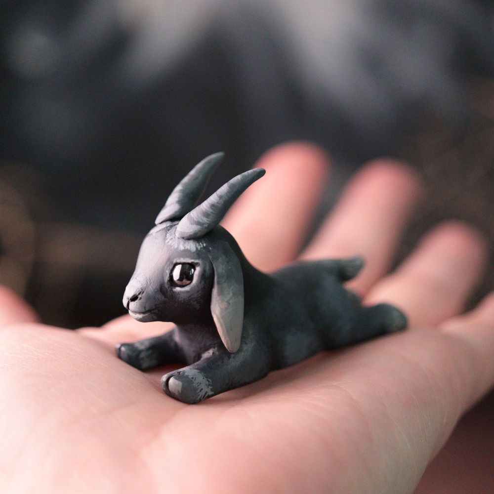 A hand holding a tiny black goat figurine 