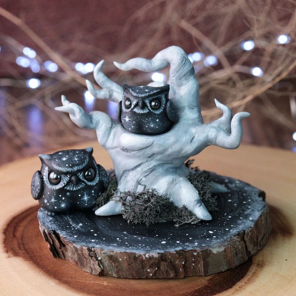 Two starry owl figurines displayed on a fantastical grey scale tree diorama 