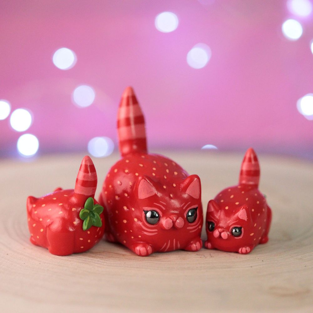Strawberry cat hybrid figurines. One is big and two are small. You can see the backside of one, which has a strawberry stem butthole