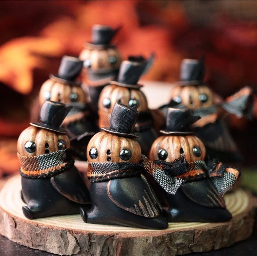 Photo of a murder of crow figurines, but they have jack-o-lantern heads with tiny top hats and scarves