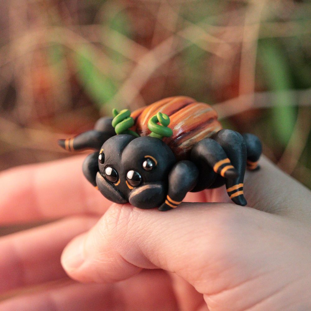 A hand holding a cute spider figurine that has a pumpkin butt