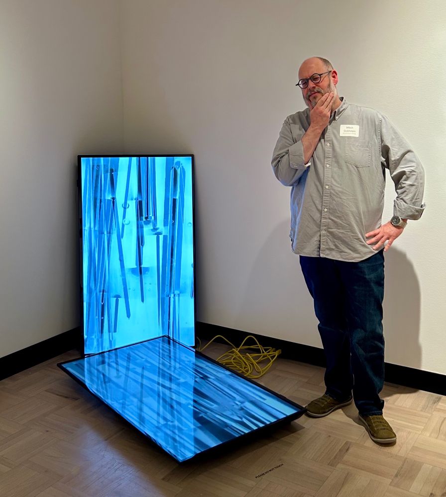 a middle aged white man looking at a piece  of contemporary video art of his own making. 