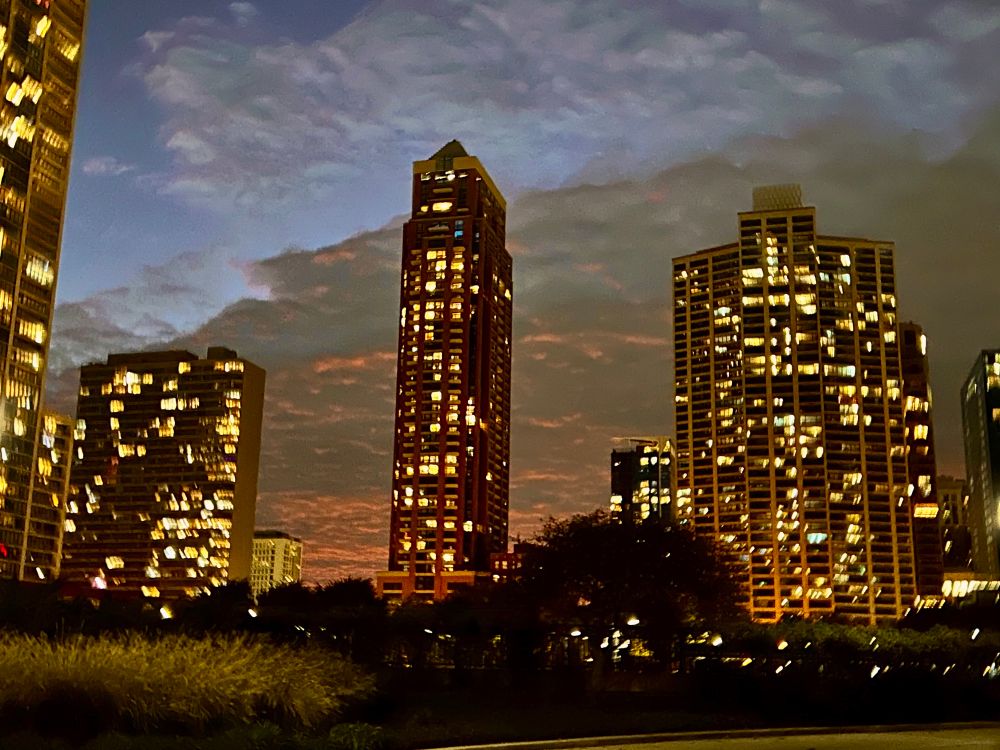 buildings lit up in yellow light, against a cloudy sky glowing orange.