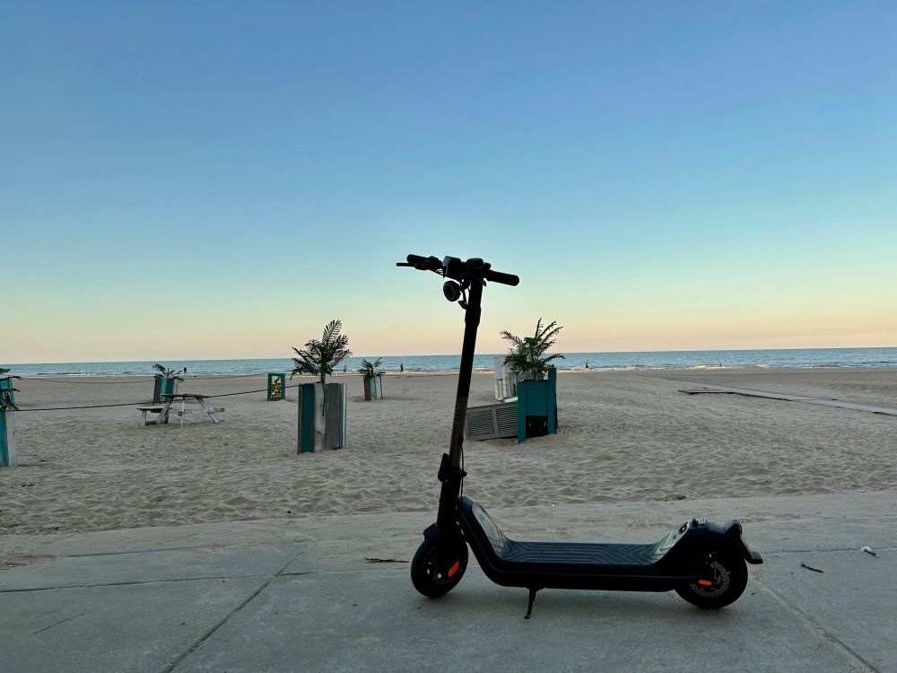 NIU KQi3 Pro electric scooter in front of a beach background at sunset.