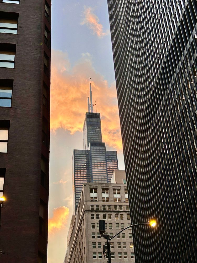 the Sears Tower seen through a gap between buildings, backlit orange and blue by the sunset sky.