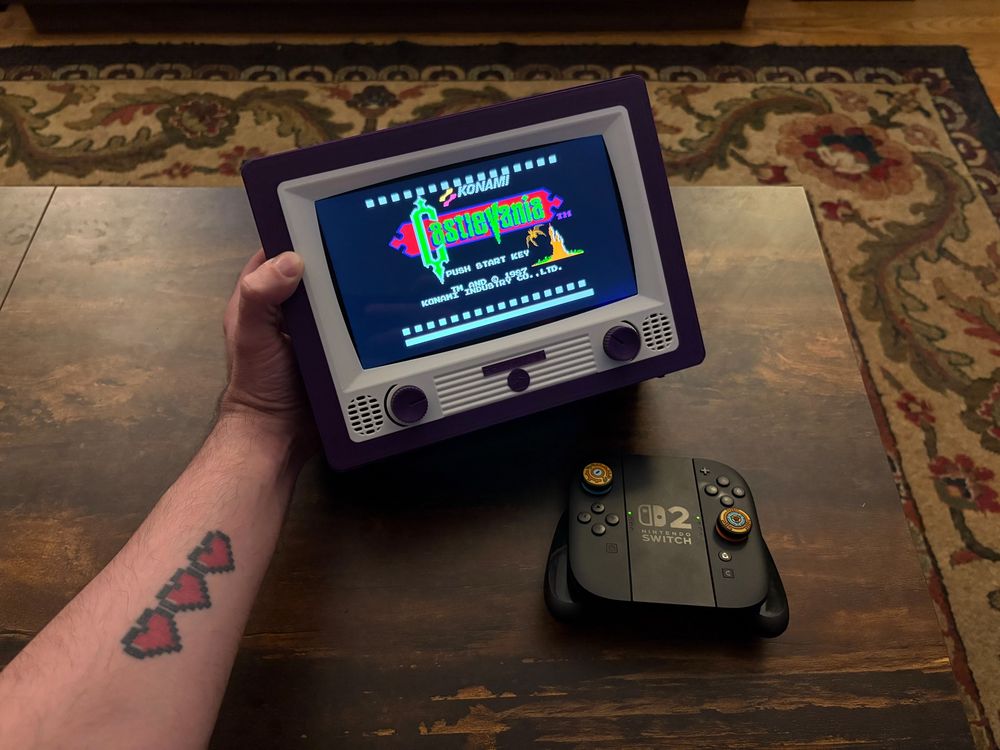 Chris’s left hand holding a PLA-printed purple and white TV casing in the style of an older CRT television with a Nintendo Switch 2 docked inside showing the Castlevania title screen for the Nintendo Entertainment System next to a Switch 2 controller.