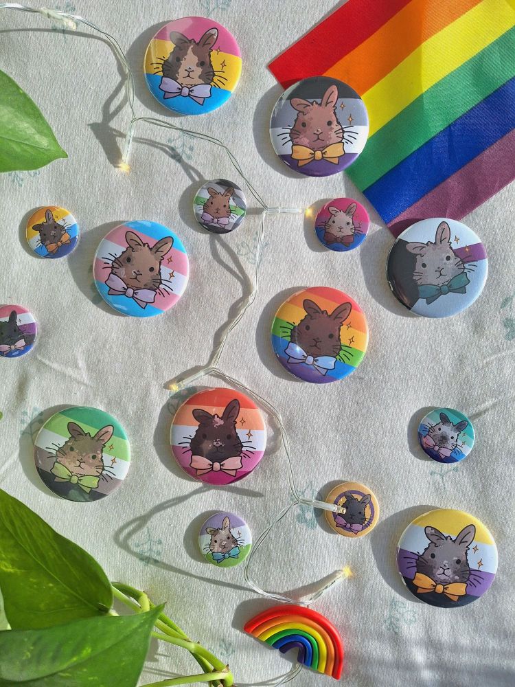 Photo of a lot of button pins with illustrated bunny faces on it. The background of the pins are different pride flags.