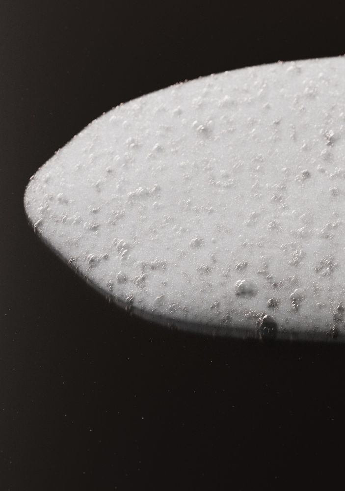 A computer generated image of white soap suds in a round puddle on a shiny black reflective surface. 