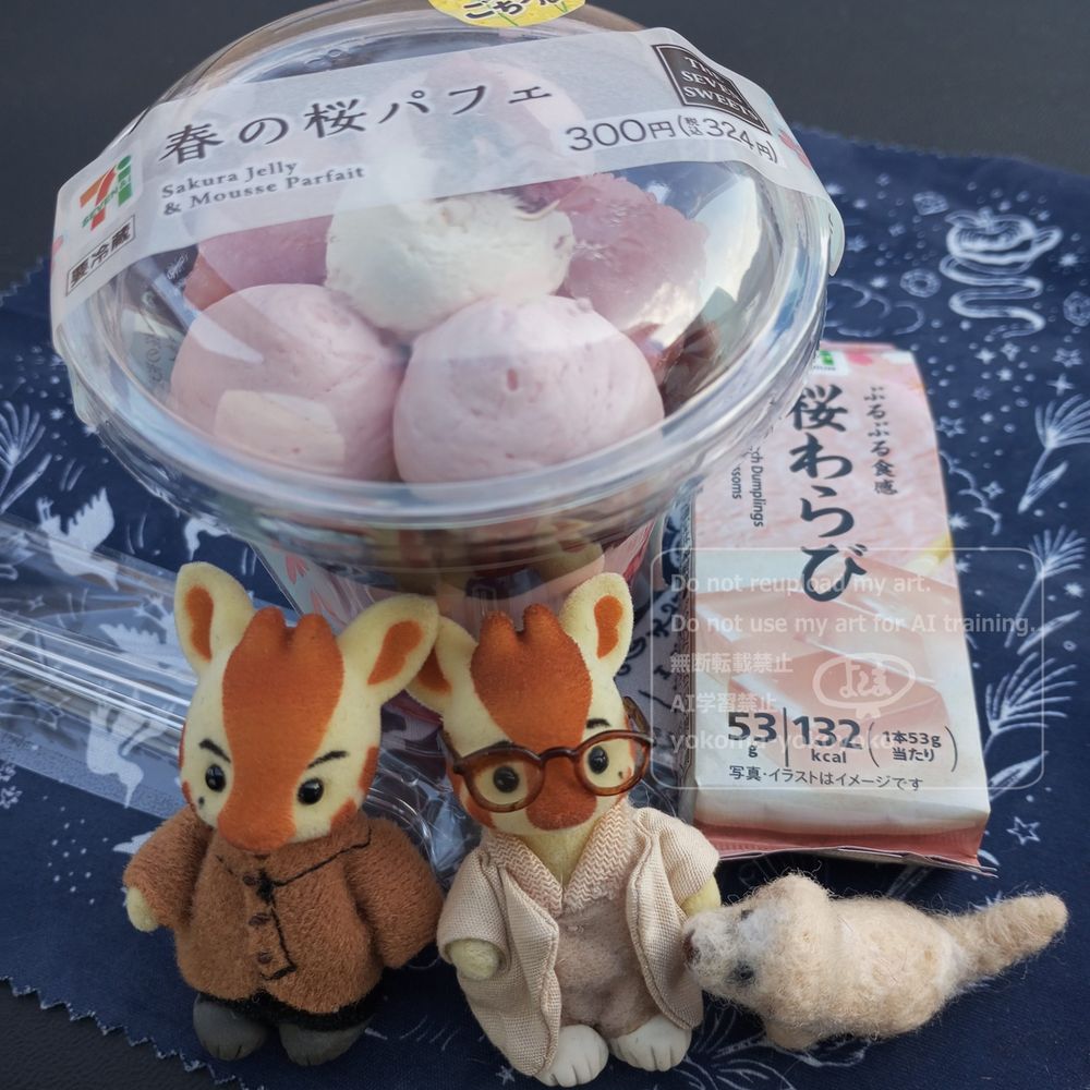 春の桜パフェと書いてあるコンビニスイーツ。ピンク色の丸く搾ったクリームが乗っている。横には桜わらびもち。カップに入ったパフェの前にキリンバニア