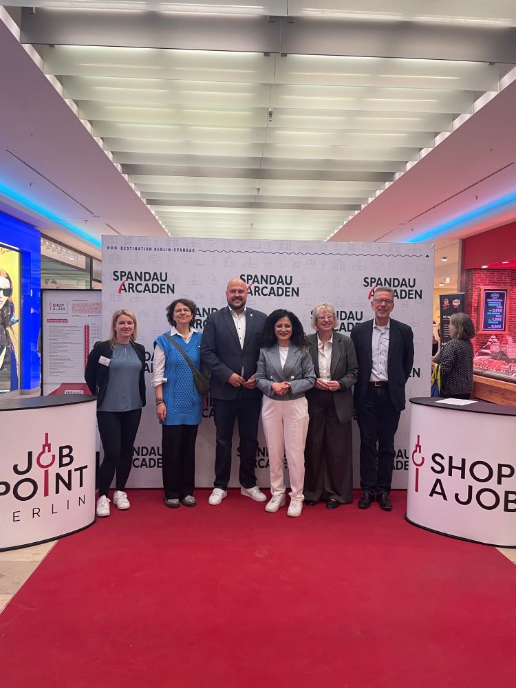 (v.l.n.r.) Denise Schütte (Leitung Messe, Arbeitgebendenservice und Stellenbörse),
Nelli Elkind (stellvertretende Geschäftsführung GesBiT gemeinnützige Gesellschaft für Bildung und Teilhabe mbH), Frank Bewig (Bezirksbürgermeister von Spandau), Cansel Kiziltepe (Senatorin für Arbeit, Soziales, Gleichstellung, Integration, Vielfalt und Antidiskriminierung), Gabriele Fliegel (Vorsitzende der Vereinigung Wirtschaftshof Spandau e.V.), Winfried Leitke (Geschäftsführer Jobcenter Berlin Spandau) stehen vor dem Hintergdund mit dem Logo von den Spandau Arcaden. Links und rechts stehen zwei Stehtische mit der Aufschrift "Shop a Job" und "Job Point Berlin". 

Foto: © JOB POINT Berlin