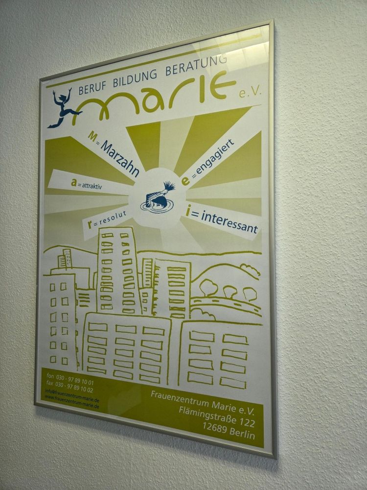 Ein Plakat an einer Wand mit dem Schriftzug „Marie e.V. – Beruf Bildung Beratung“. Es zeigt stilisierte Gebäude und benennt Eigenschaften wie „Marzahn“, „attraktiv“, „resolut“, „interessant“ und „engagiert“. Unten stehen die Kontaktdaten des Frauenzentrums.
