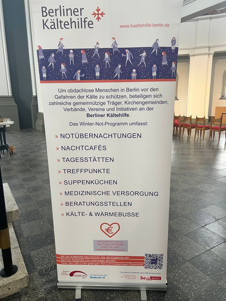 Ein Rollup der Berliner Kältehilfe mit dem Logo und dem Text:
"Um obdachlose Menschen in Berlin vor den Gefahren der Kälte zu schützen, beteiligen sich zahlreiche gemeinnützige Träger, Kirchengemeinden, Verbände, Vereine und Initiativen an der Berliner Kältehilfe.

Das Winter-Not-Programm umfass

- Notübernachtungen
- Nachtcafés
- Tagesstätten
- Treffpunkte
- Suppenküchen
- Medizinische Versorgung
- Beratungsstellen 
- Kälte- und Wäremebusse 

www.kaeltehilfe-berlin.de"