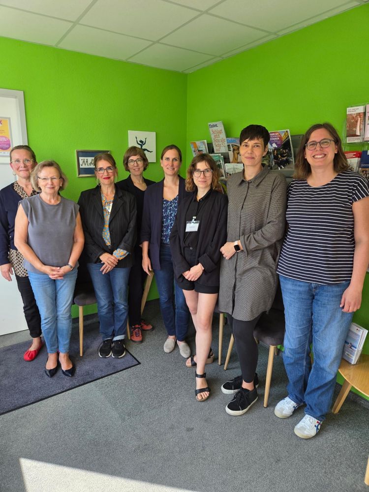 Gruppenfoto von acht Frauen vor einer knallgrünen Wand mit Informationsbroschüren. Sie stehen eng beieinander, lächeln in die Kamera und wirken kollegial und zugewandt.
Abgebildet sind u.a.: 
3.v.l.: Nina-Sybil Klüppel (Geschäftsführerin Frauenzentrum Marie e.V.);
4.v.l.: Manja Finnberg (Koordinatorin für Alleinerziehende in Marzahn-Hellersdorf);
5. v.l.: Micha Klapp (Staatssekretärin für Arbeit und Gleichstellung);
6.v.l.: Krzysztofa Beniak (Beraterin im Frauenzentrum Marie e.V.);
7.v.l.: Stefanie Schams (Anlaufstelle für Alleinerziehende in Marzahn-Hellersdorf)