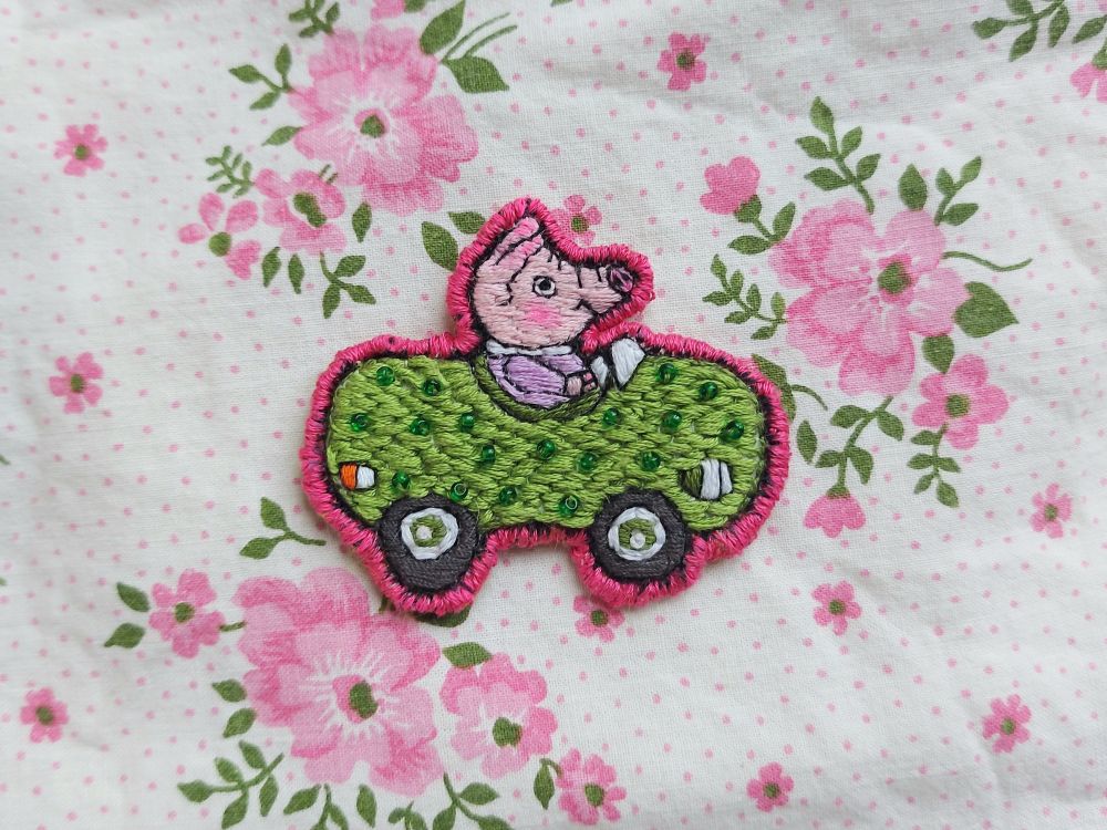 embroidered green pickle car patch from richard scarry's busytown photographed on top of my cute flowery bedsheets