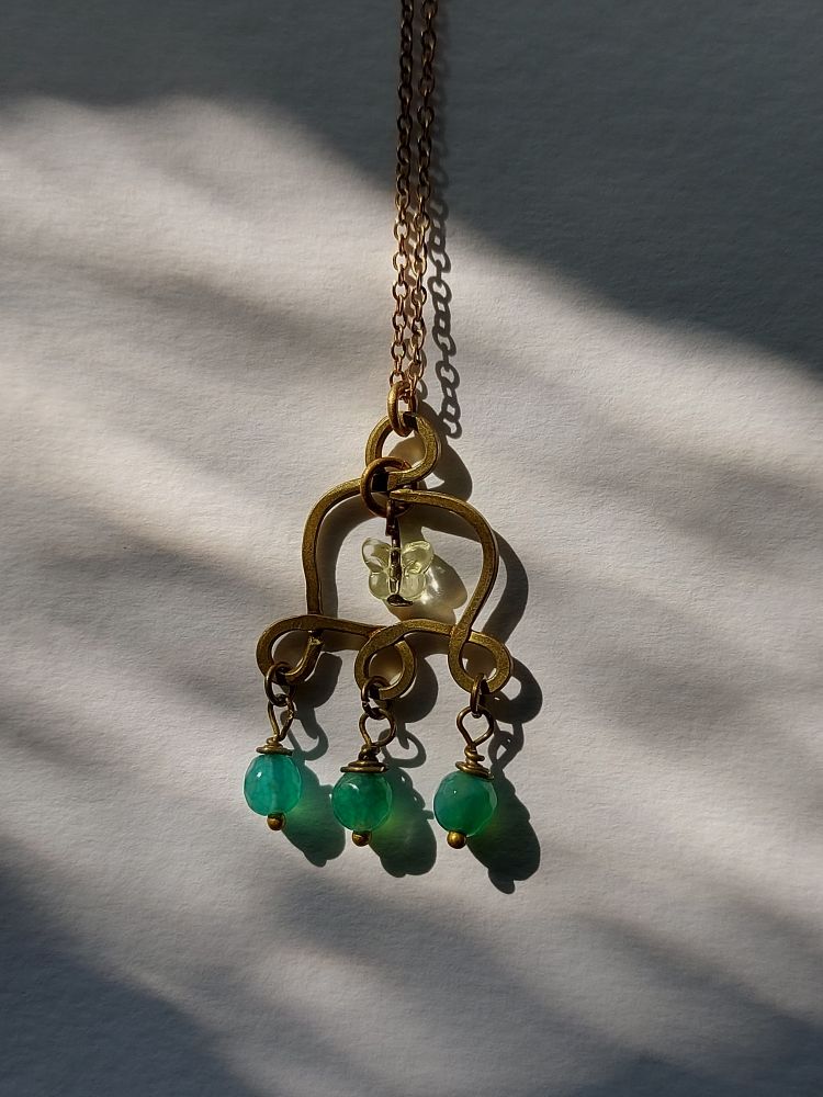 a bell shaped brass pendant with beads on it, one of them shaped like a butterfly