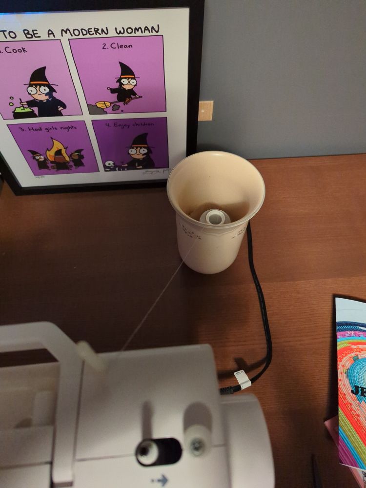 A cone of silver thread in a heavy vase behind the sewing machine.