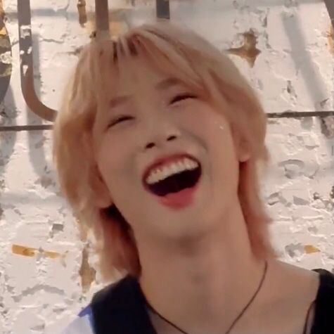 Hu Yetao has light pink fluffy hair and is smiling widely with his mouth open and his eyes almost closed. His head is turning back. 