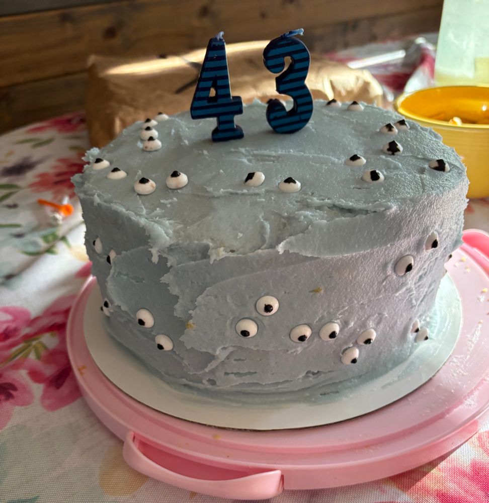 A cake frosted with blue frosting with eyeball candies placed randomly all over it 