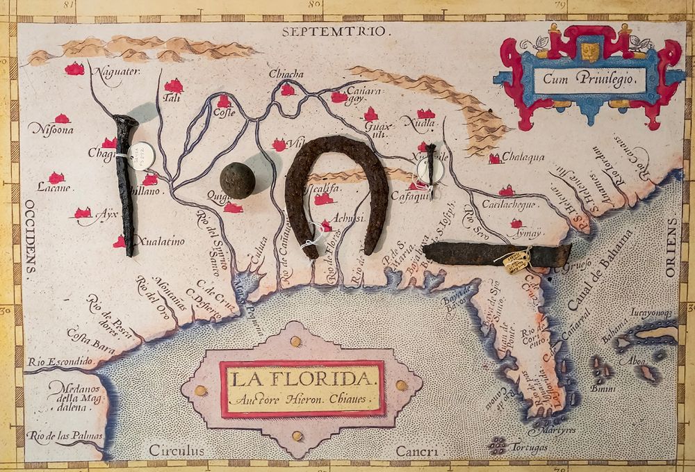 an old vintage map of La Florida and the southeastern united states has several iron artifacts resting on it like a horseshoe and big nails