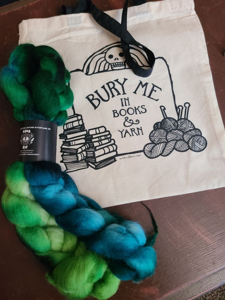 A blue green braid of dyed Shaniko wool and a canvas tote that says "bury me in books and yarn"