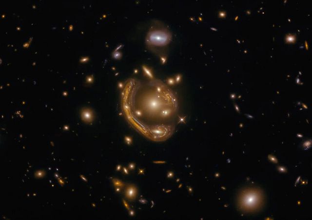 An Einstein Ring. Gravitational lensing causes light from a distant galaxy to be warped by a closer galaxy. Studying the amount of gravitational lensing that we can see versus how much we should expect is a great tool for cosmologists trying to understand the origins and fate of our universe.
Image Credit: Wikimedia Commons.