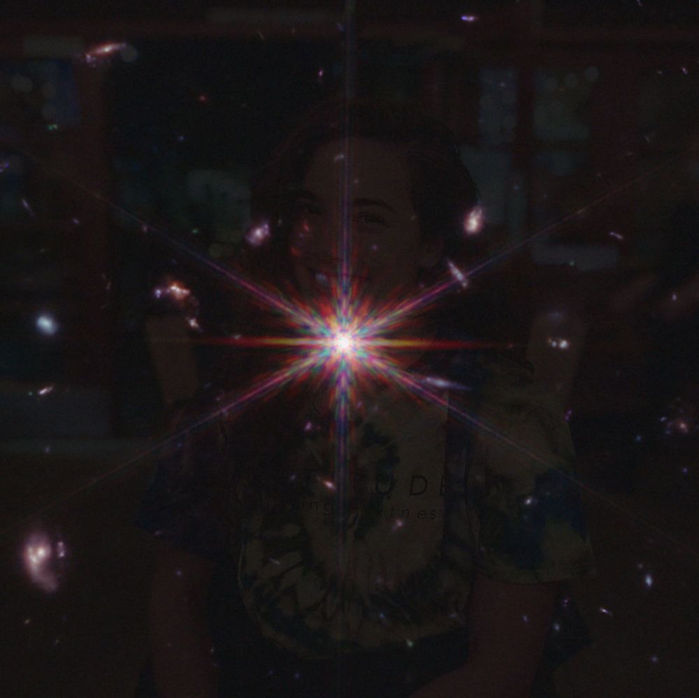 An image of a bright point of reddish light surrounded by 6 emanating rays of light with an image of a woman faintly superimposed