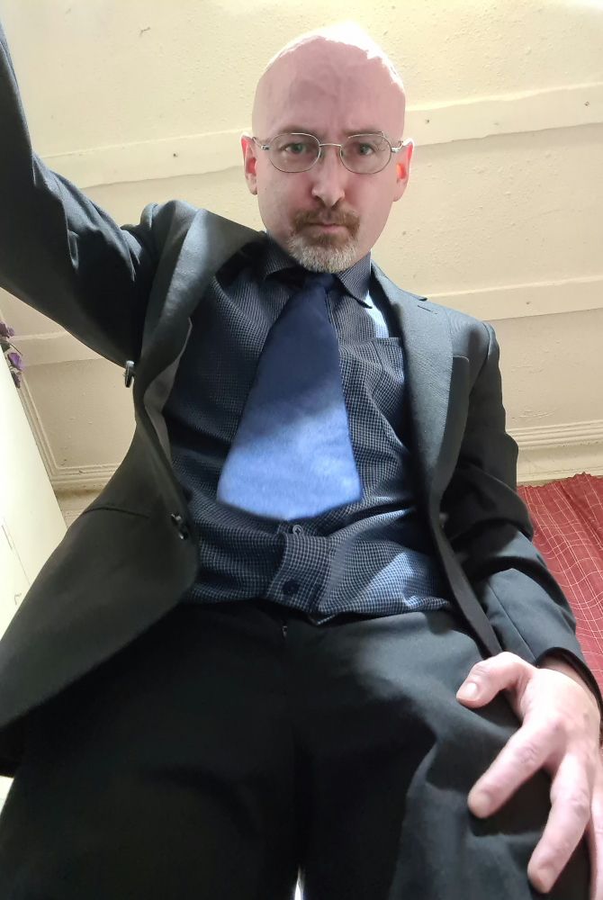 Spen is leaning forward in a dark suit opening the lid of your pet cage, his hand is close to his bulge, highlighting how hard he is getting for you