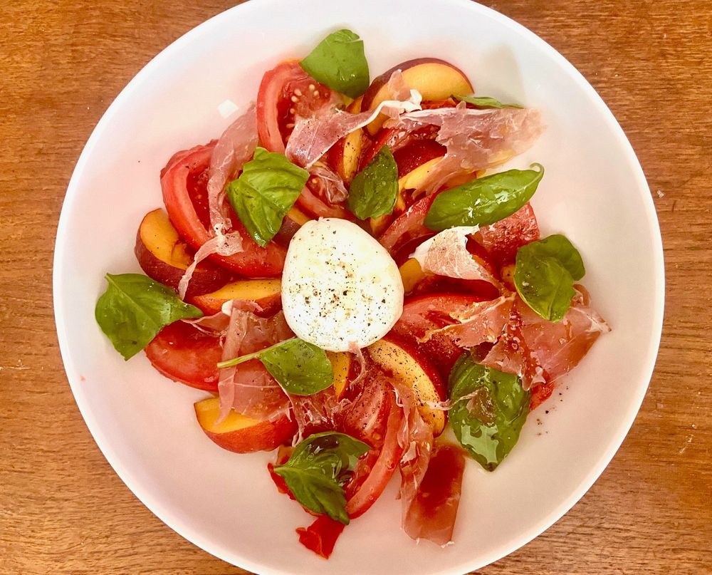slices of peaches, tomatoes, torn pieces of prosciutto and basil, a ball of burrata in the middle of a round bowl. 