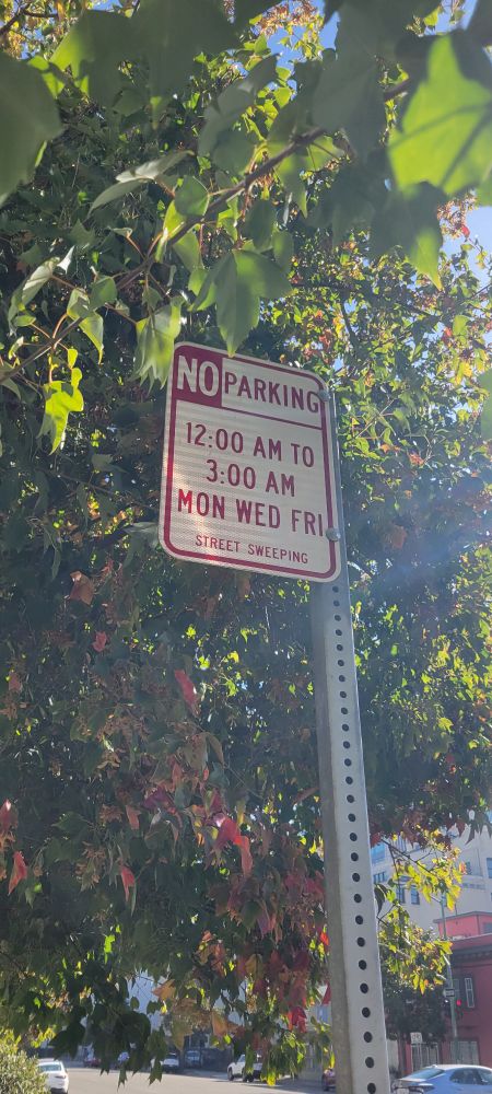 A street sign that says " NO parking 12:00am to 3:00am MON WED FRI 
Street sweeping "