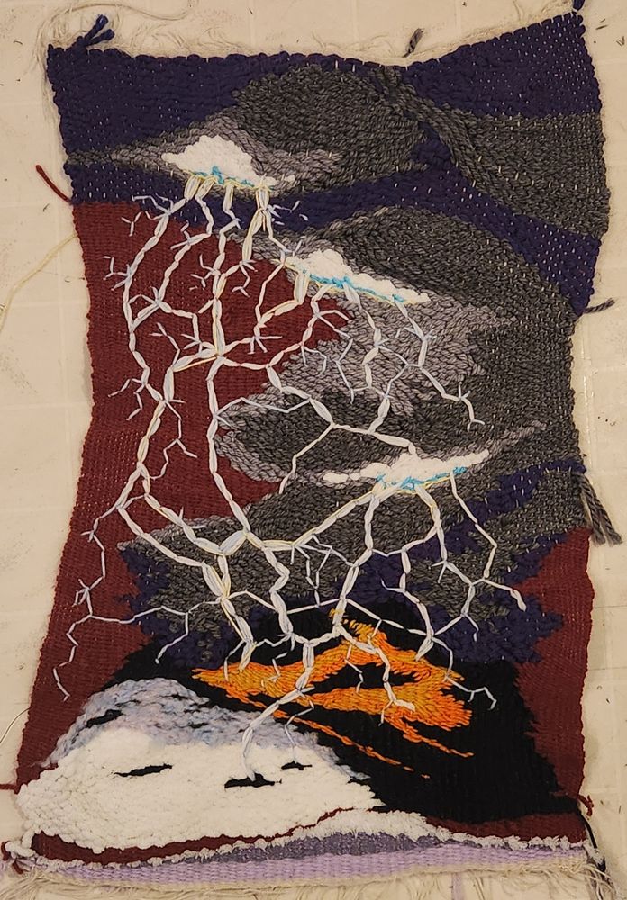 A woven thing of an erupting volcano with lightning strinking from the dark clouds above