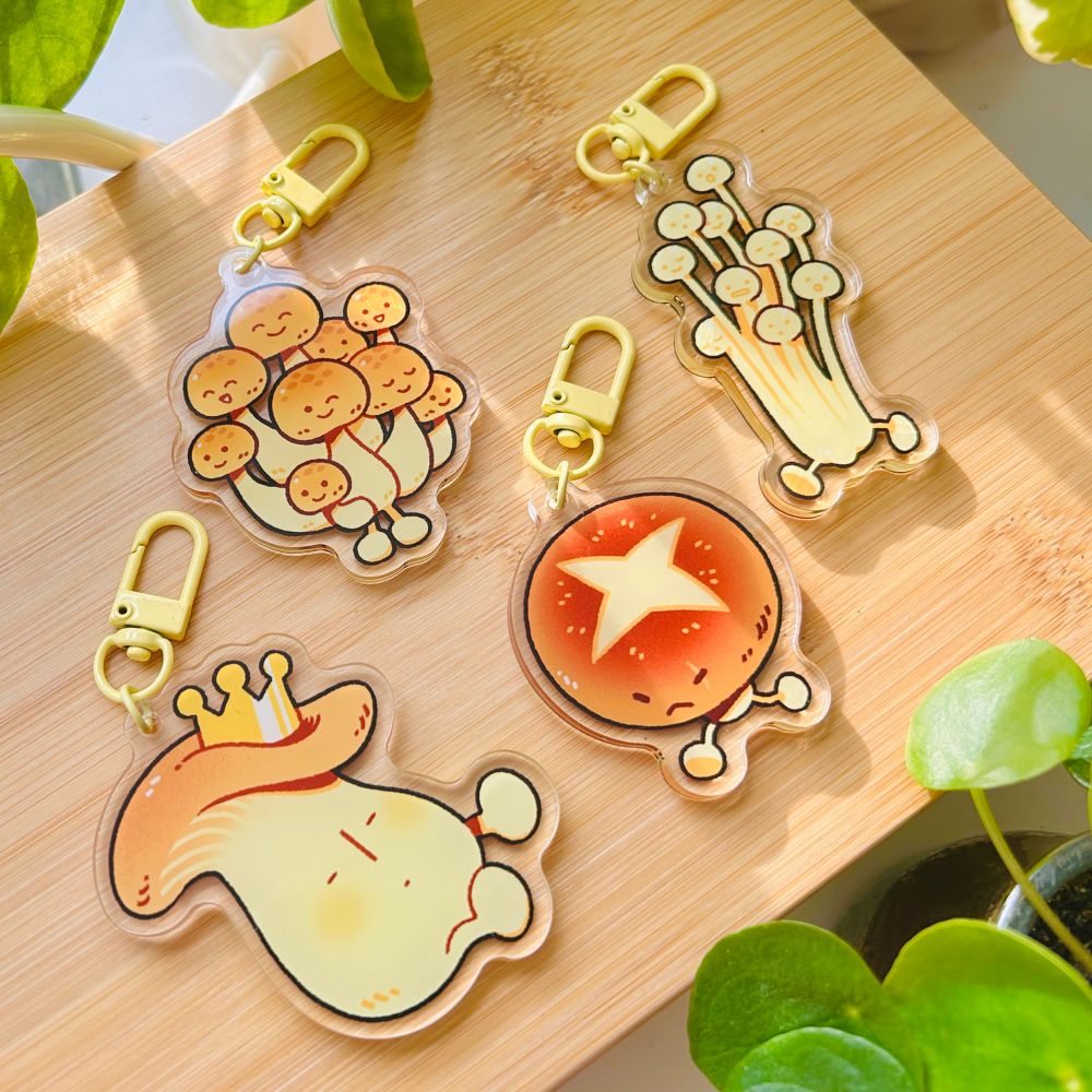 i turned my mushrooms into charms!! little cartoonified mushroom pals featuring king oyster with a crown, shimeji, shiitake with a cut scar on its cap, and tall enoki. each mushroom has a face or multiple faces on it as well as a little pair of legs.