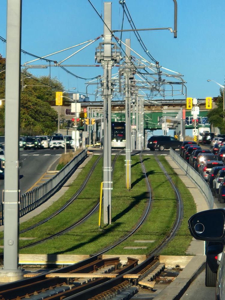 Picture taken from a car in a busy left-turn lane on Eglinton Avenue at Leslie, of a train of the Eglinton Crosstown waiting at a red light.