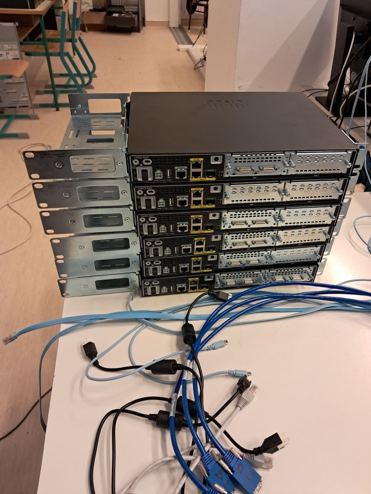 Six Cisco 4221 routers stacked on each other on a gray desk