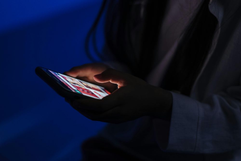 Eine Person hält ein Smartphone in den Händen. Um sie herum ist es dunkel.